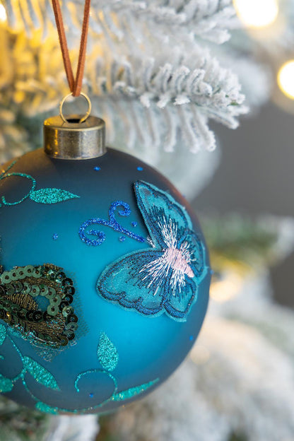 Glass Christmas ball ornament, blue with teal butterfly and glitter, hung by brown cord on tree on Tampa Home & Garden Store