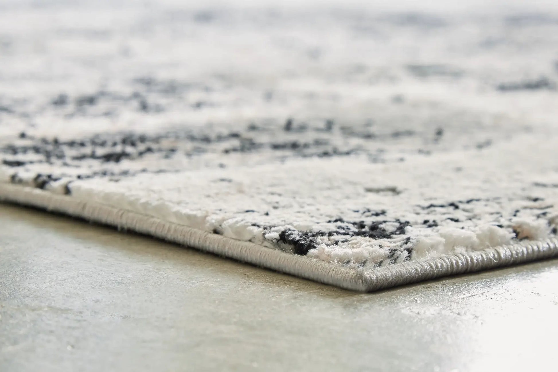 Langwell rug, gray-black tonal pile with beige edge binding, close-up on concrete floor on Tampa Home & Garden Store