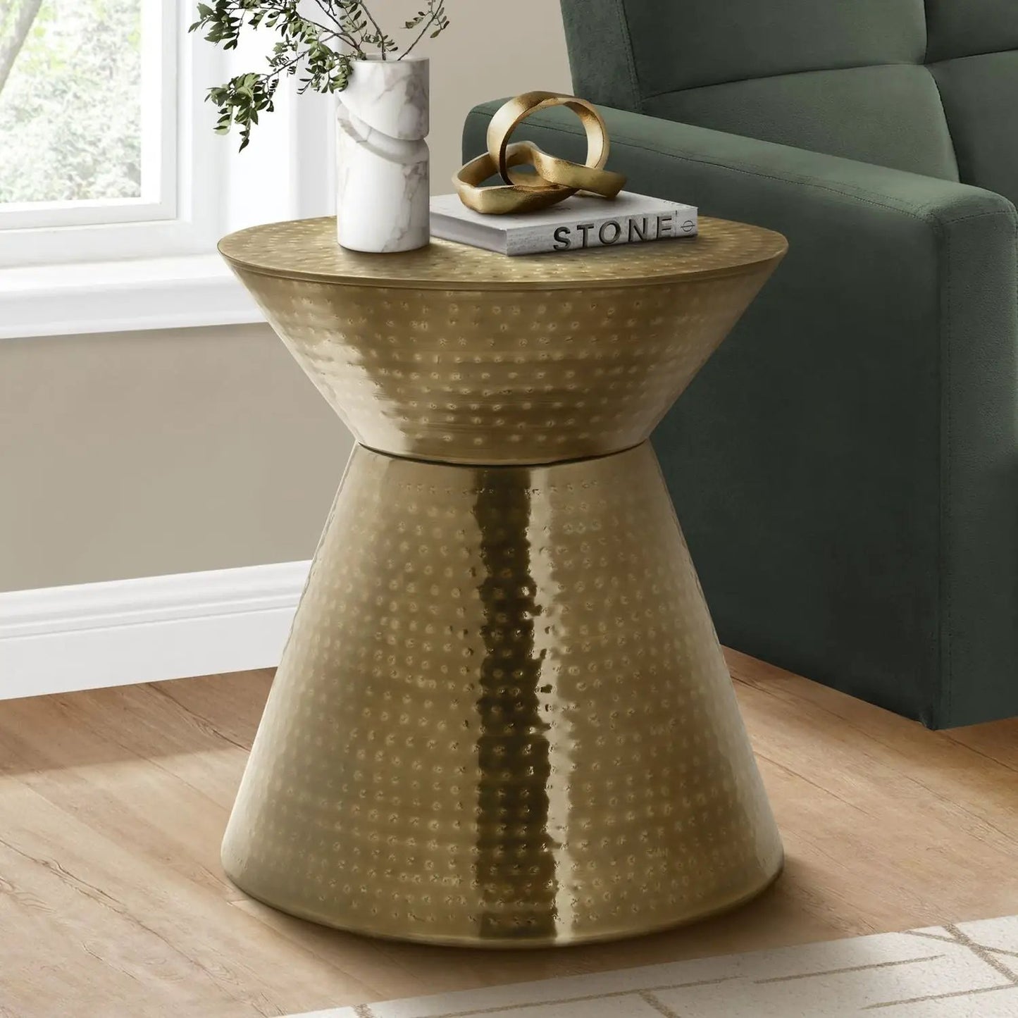Gold hammered drum side table beside a green sofa; marble vase, Stone book, gold sculpture on Tampa Home & Garden Store