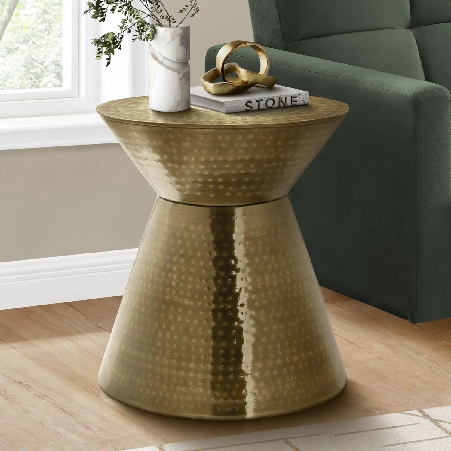 Gold hammered drum side table beside a green sofa; marble vase, Stone book, gold sculpture on Tampa Home & Garden Store