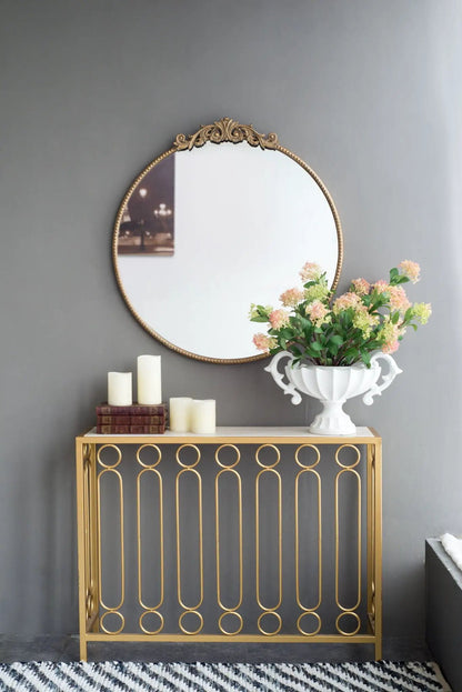 Round wall mirror with ornate gold Baroque frame and crest over a circular-motif console on Tampa Home & Garden Store