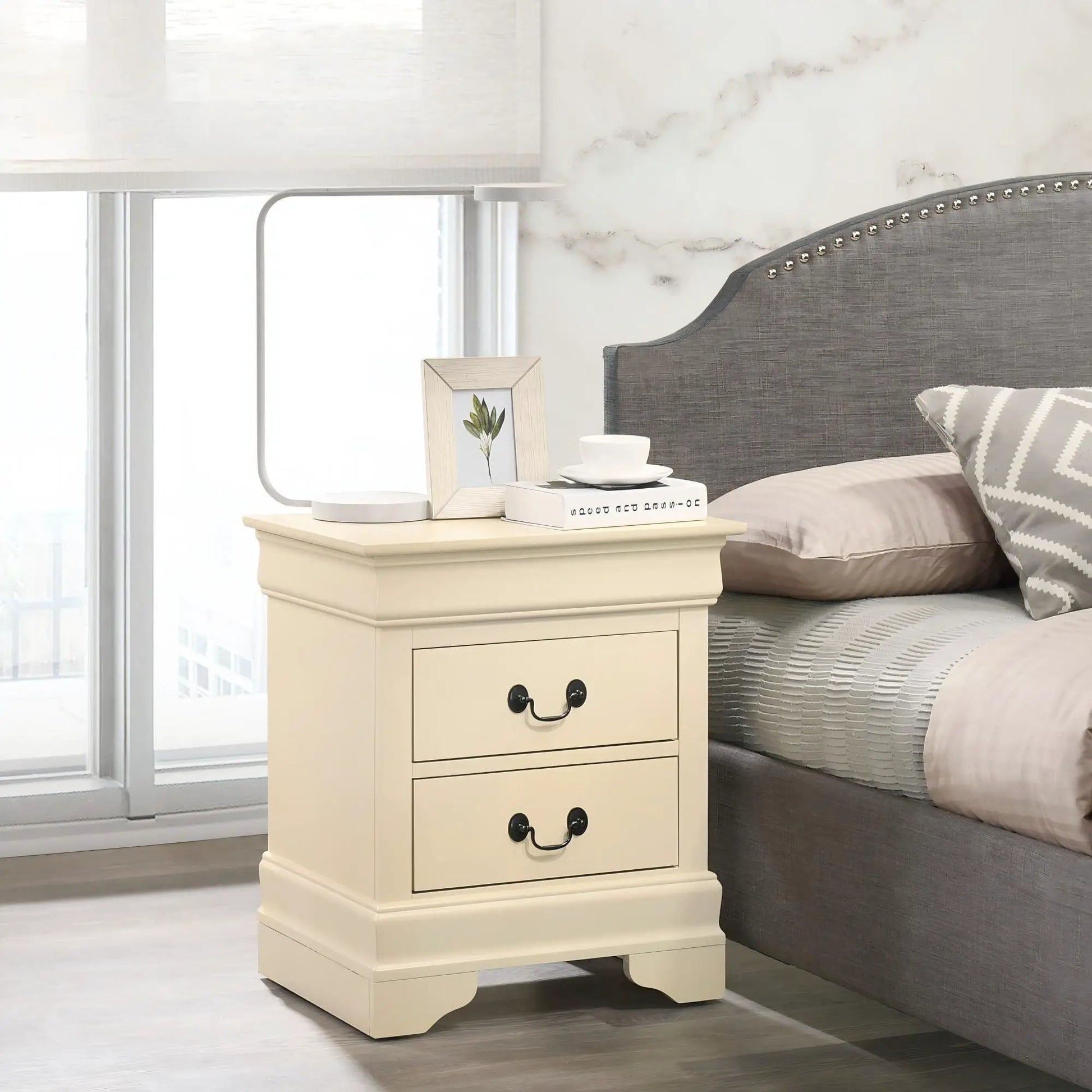 Traditional cream nightstand with 3 drawers, curved base, black pulls beside a gray bed on Tampa Home & Garden Store