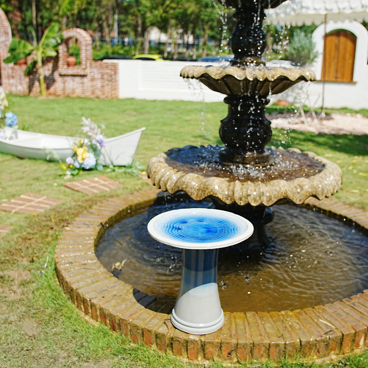 Handmade glazed ceramic bird bath by HouseOfZazla atop a black pedestal fountain in a garden on Tampa Home & Garden Store