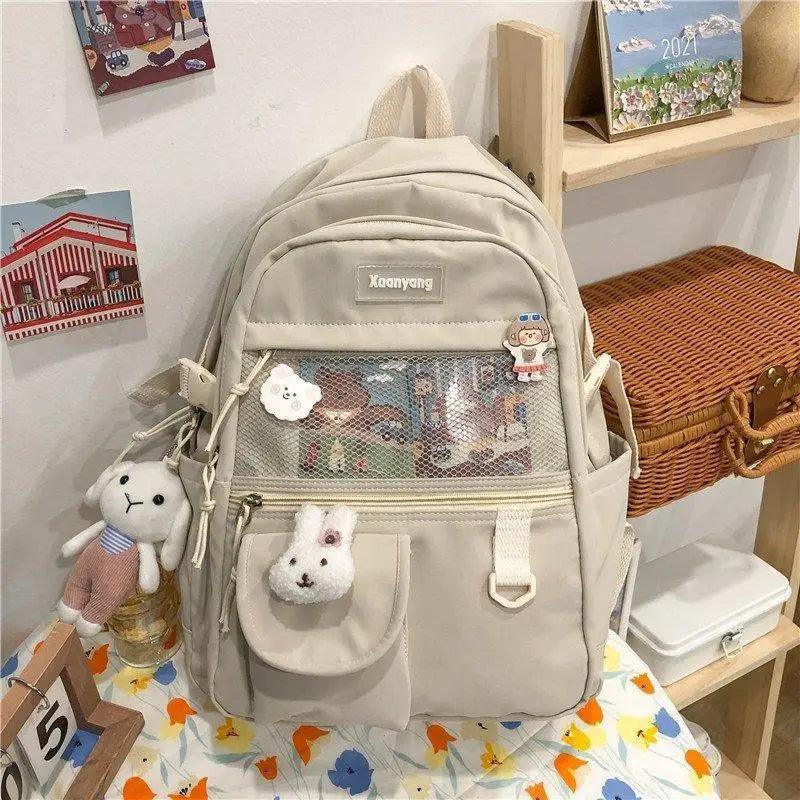 Beige Stevvex school backpack with front mesh pocket, two side pockets, and two plush keychains on Tampa Home & Garden Store