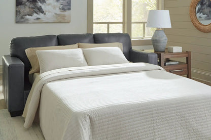 Bolsena sofa sleeper in dark gray leather with beige bedding in a bright bedroom on Tampa Home & Garden Store