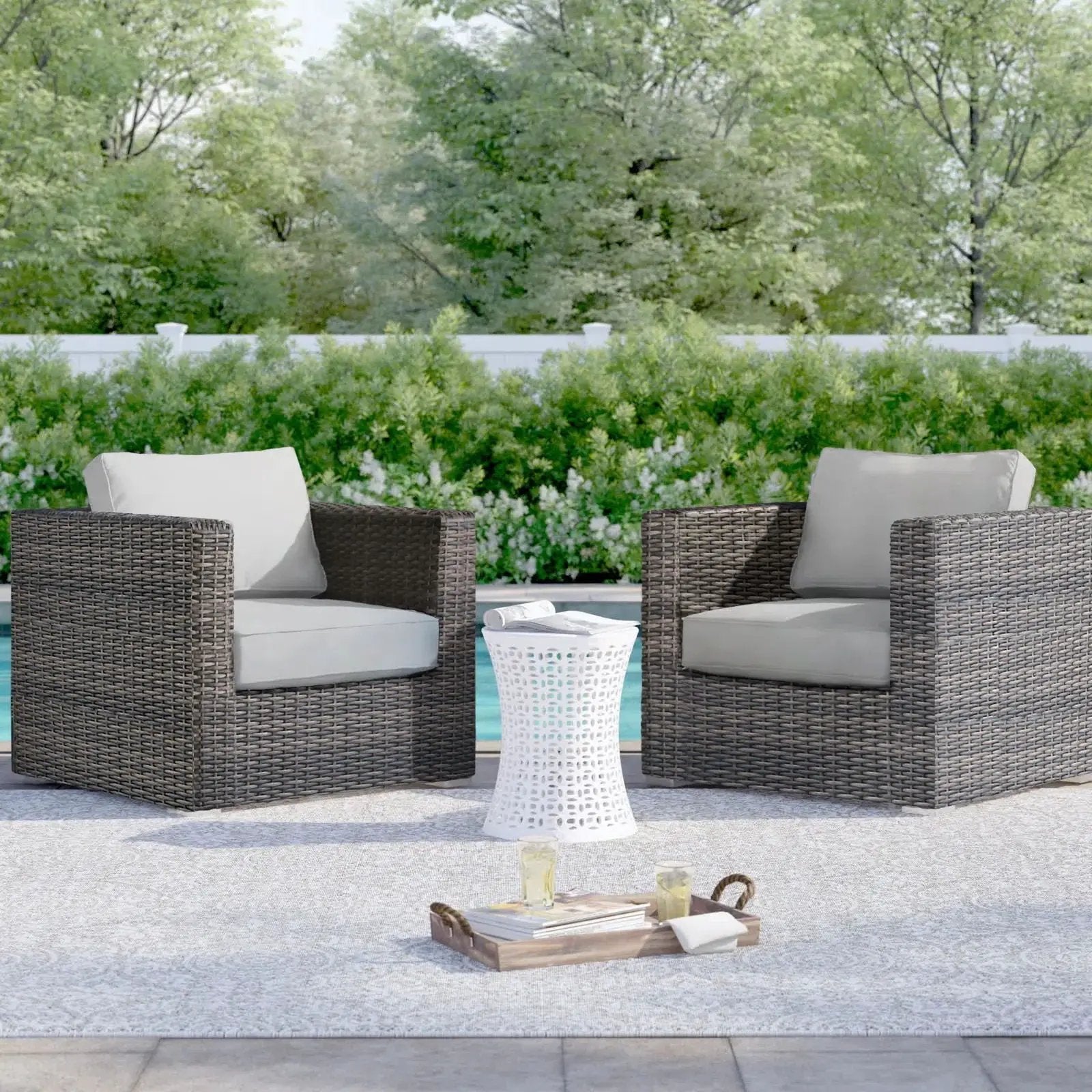 Two dark brown wicker patio arm chairs with beige cushions and a white lattice table by pool on Tampa Home & Garden Store