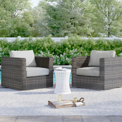 Two dark brown wicker patio arm chairs with beige cushions and a white lattice table by pool on Tampa Home & Garden Store