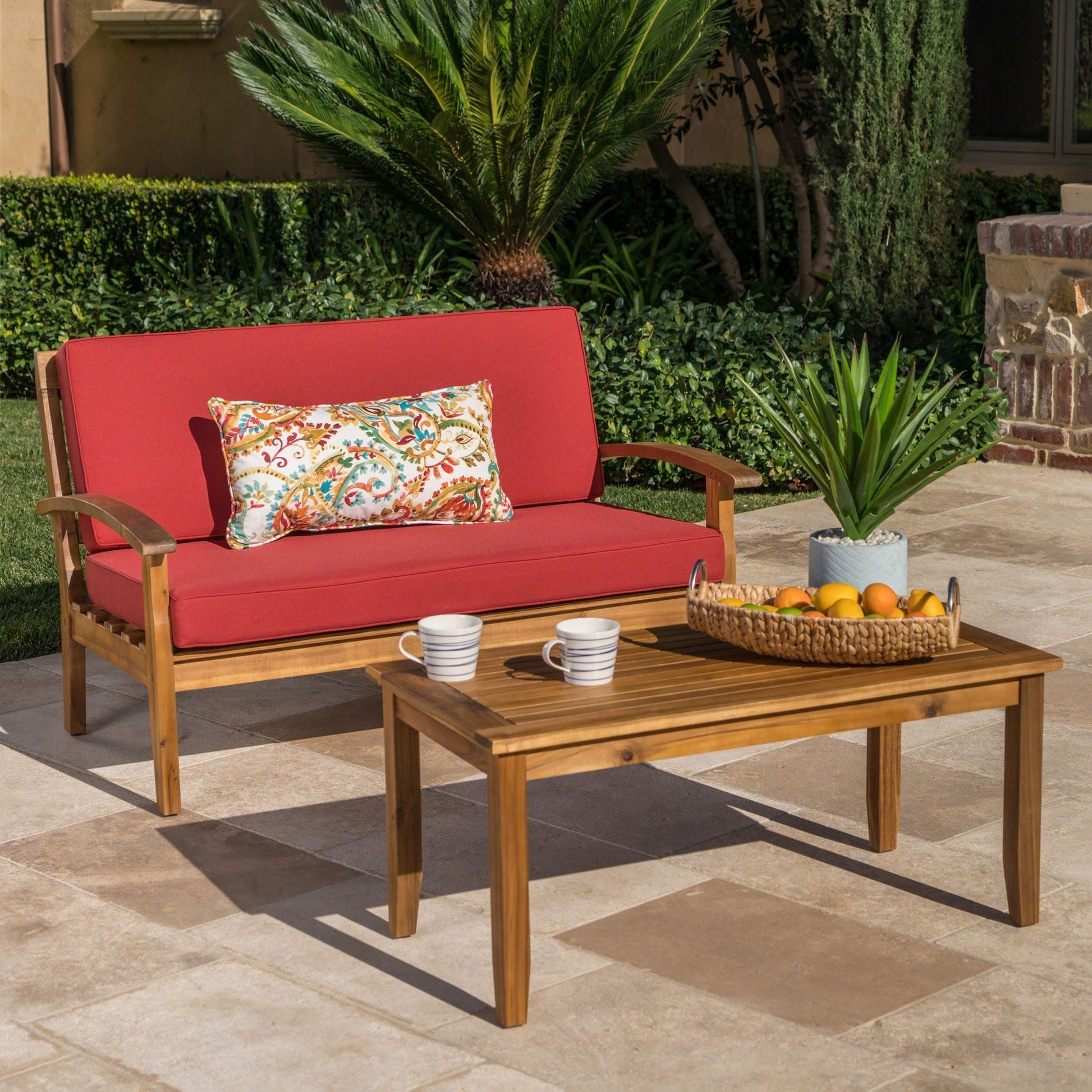 Outdoor chat set with red cushioned loveseat and wooden coffee table on a patio with a pillow on Tampa Home & Garden Store