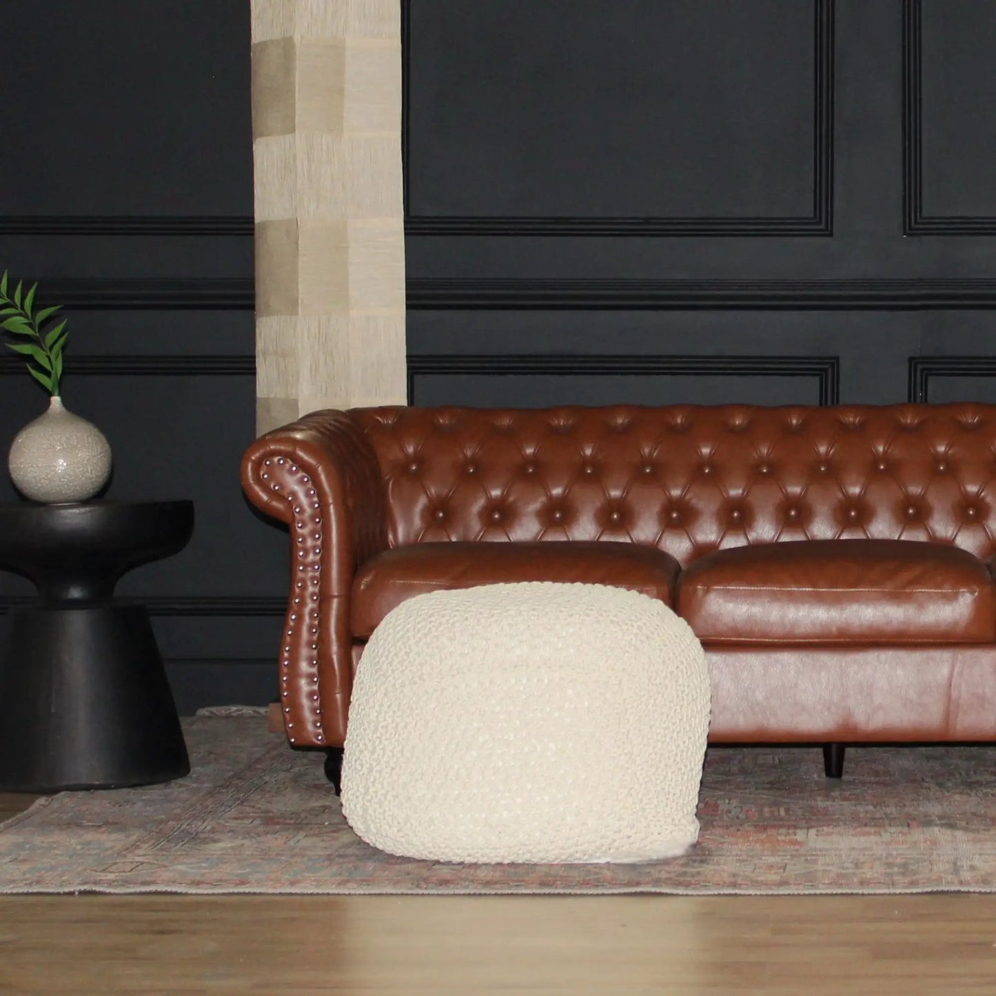 Semi rounded cable knitted pouf in beige beside a brown leather Chesterfield sofa on Tampa Home & Garden Store