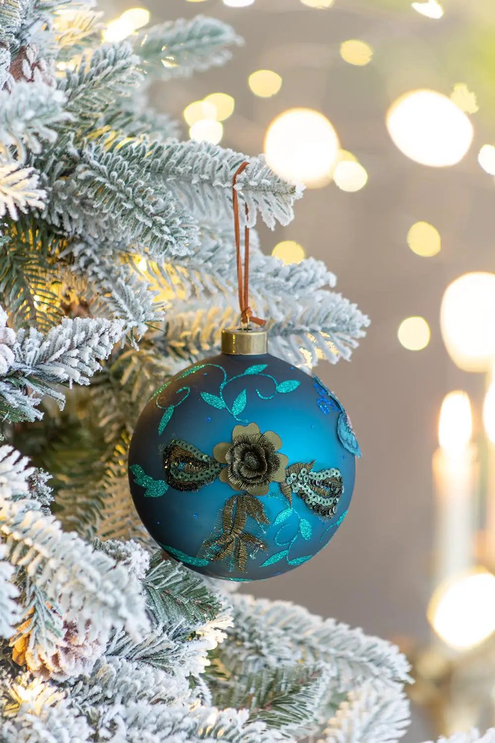 Glass Christmas ball ornament with teal accents and gold cap hanging on frosted pine branch on Tampa Home & Garden Store