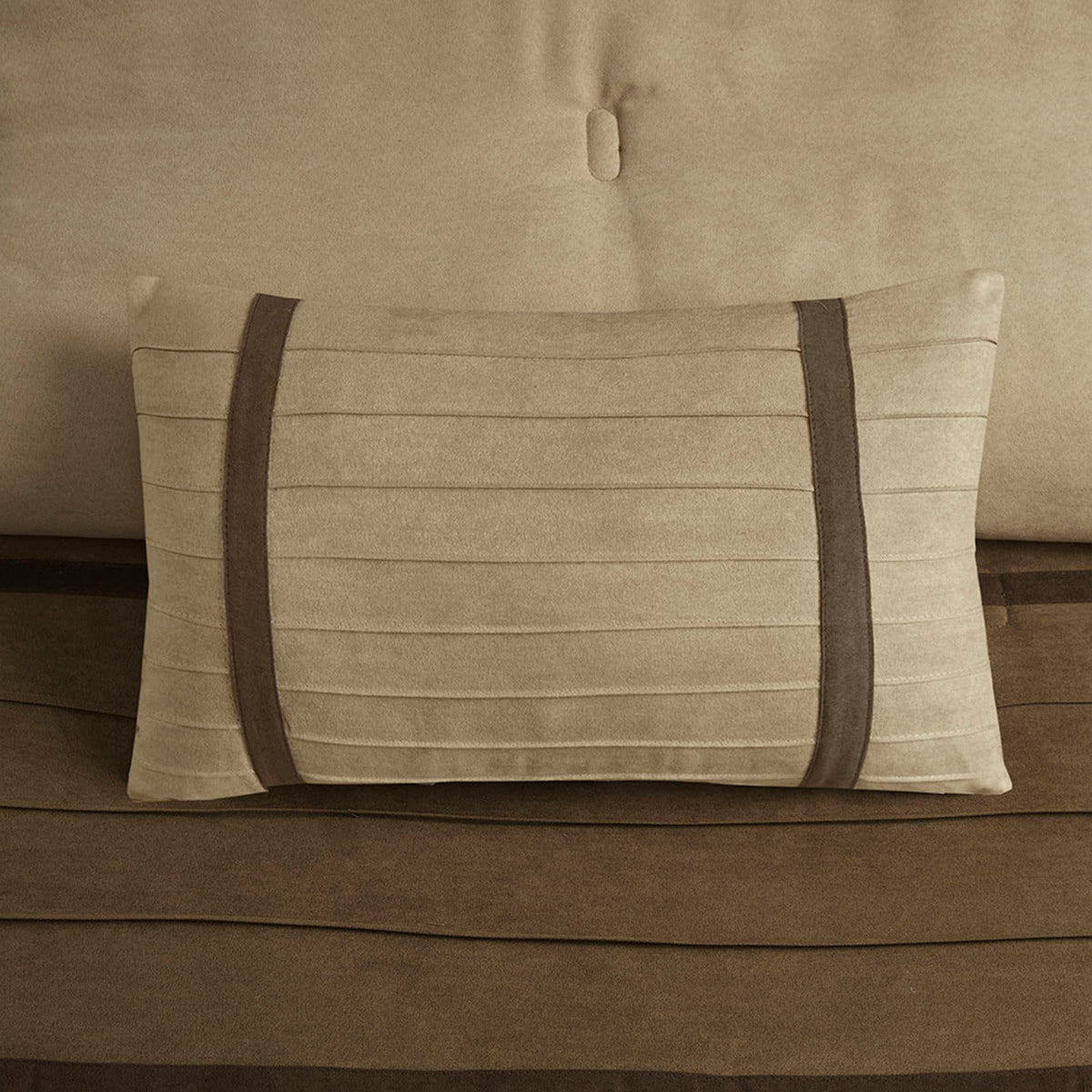 Decorative beige pillow with two dark brown faux suede straps on a brown bedspread on Tampa Home & Garden Store