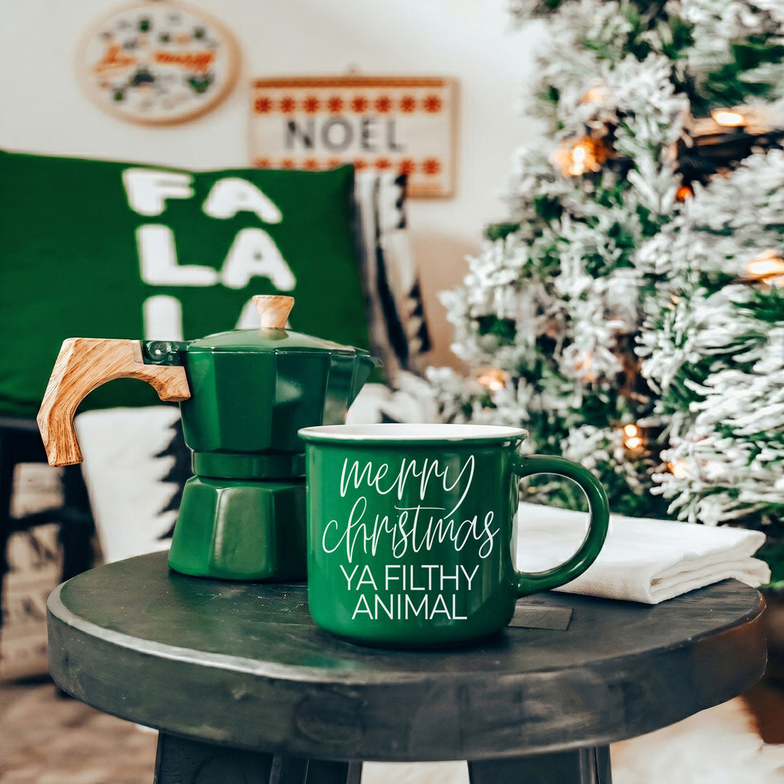 Green ceramic mug with Merry Christmas Ya Filthy Animal text beside a green moka pot on a table on Tampa Home & Garden Store
