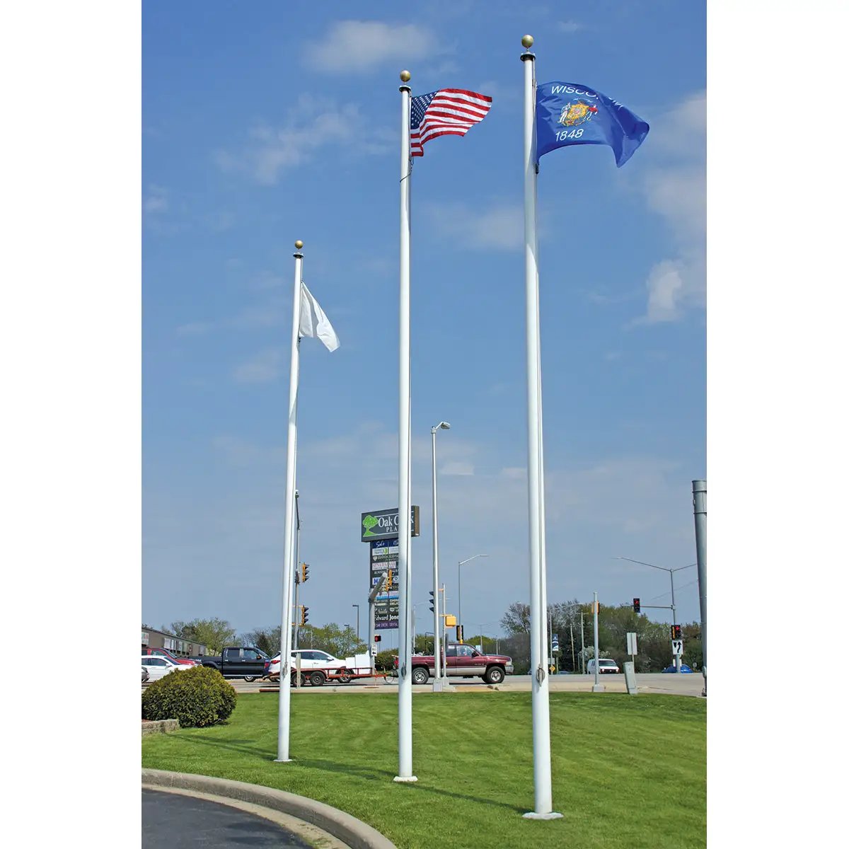 Three aluminum flagpoles with white, US, and Wisconsin flags on a grassy median on Tampa Home & Garden Store