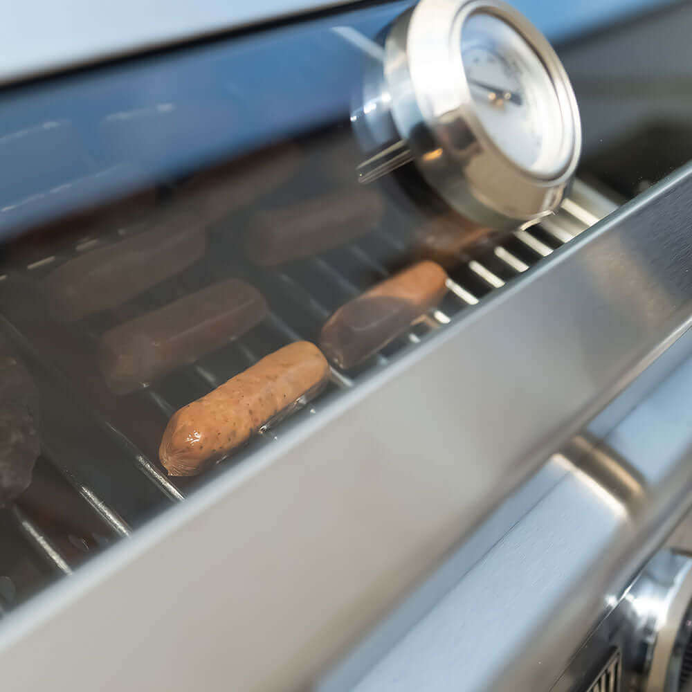 G22 Monument Grills stainless steel tabletop grill with thermometer; two sausages on grate on Tampa Home & Garden Store
