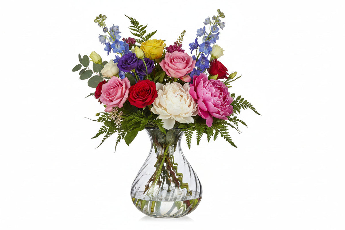 Wavy clear glass vase with a colorful bouquet of roses, peonies, delphiniums and ferns on Tampa Home & Garden Store