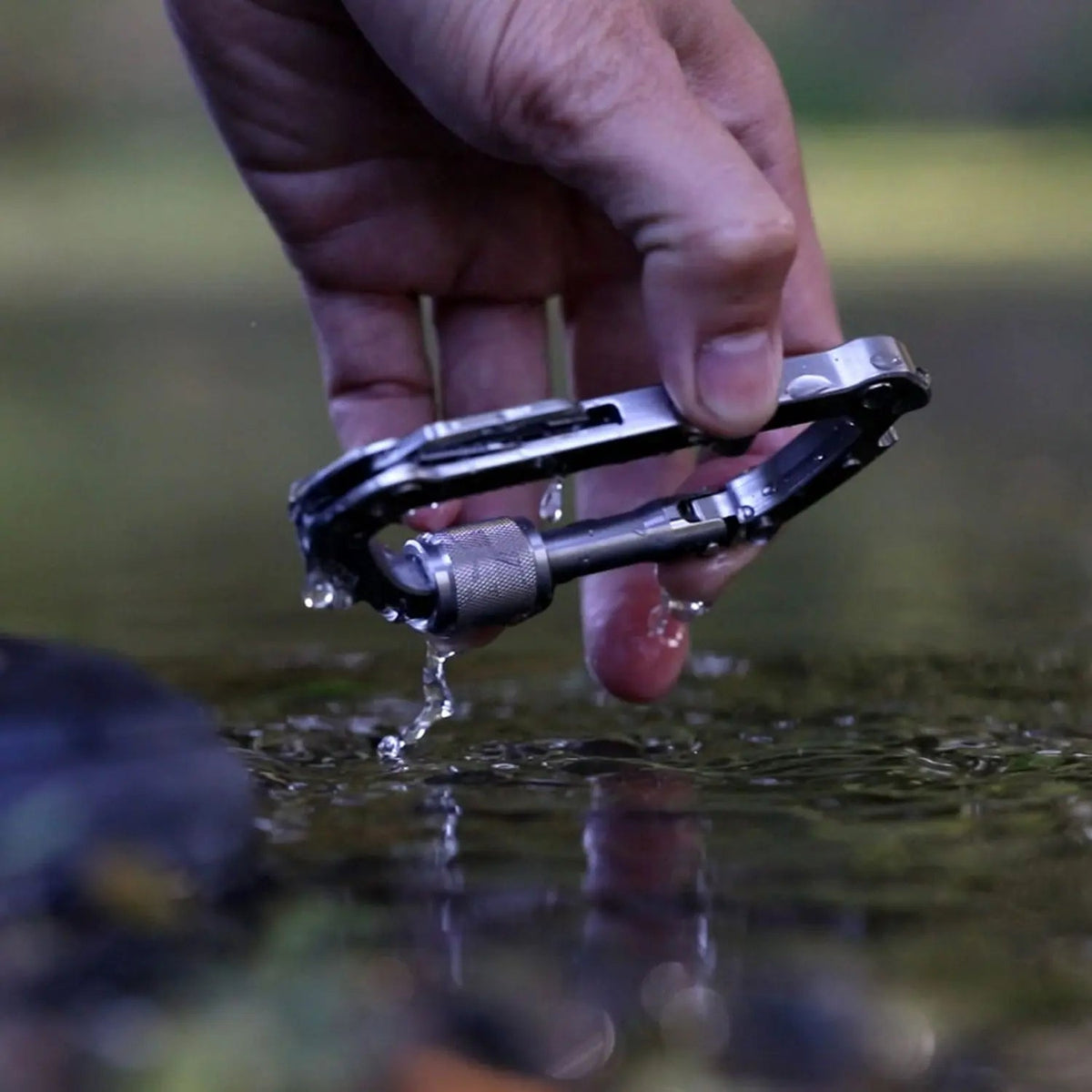 GPCA Carabiner PRO EDC multitool clip in silver metal held between fingers above water on Tampa Home & Garden Store