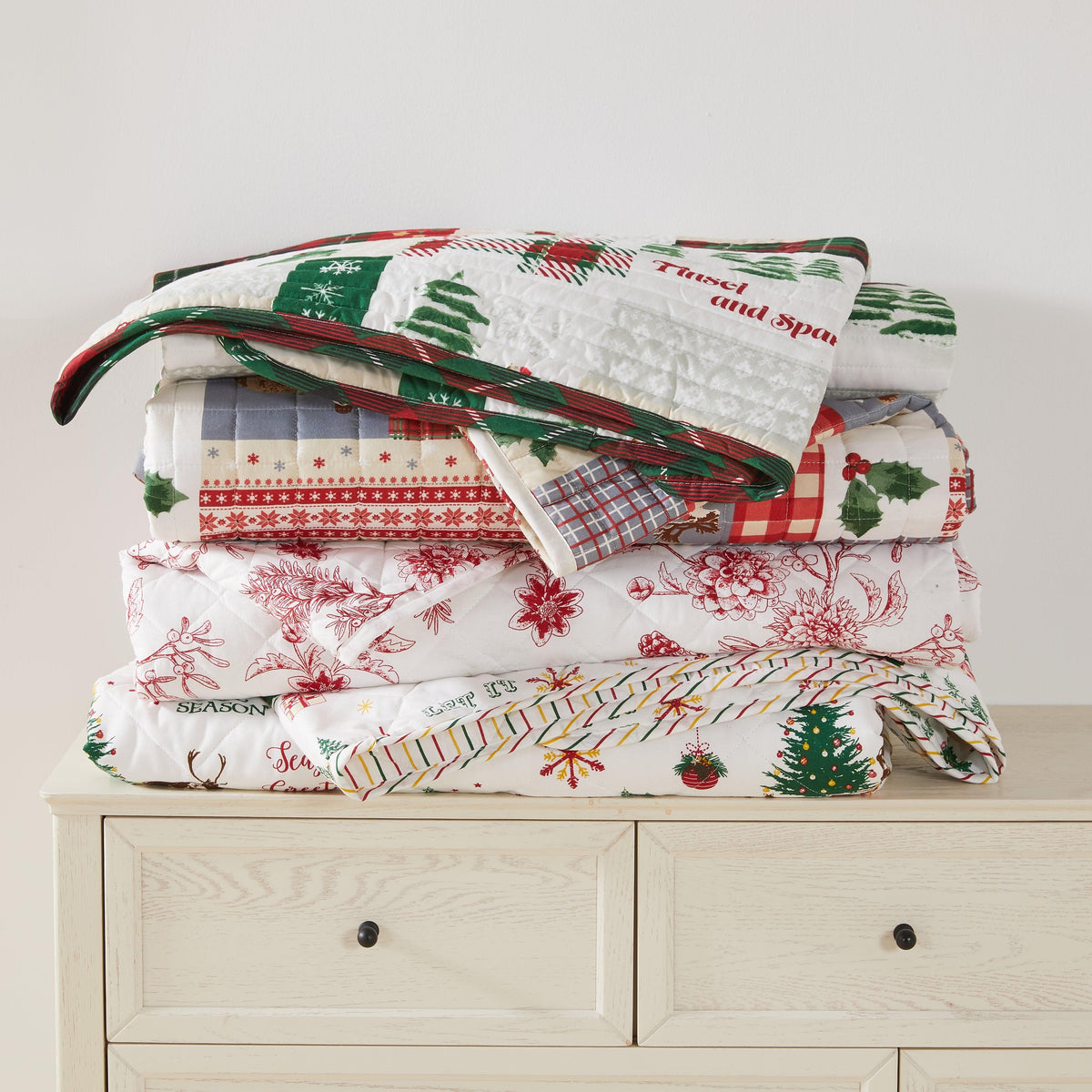 Colorful Holiday Quilt by Great Bay Home, Midnight Magic; red and green prints stacked on dresser on Tampa Home & Garden Store