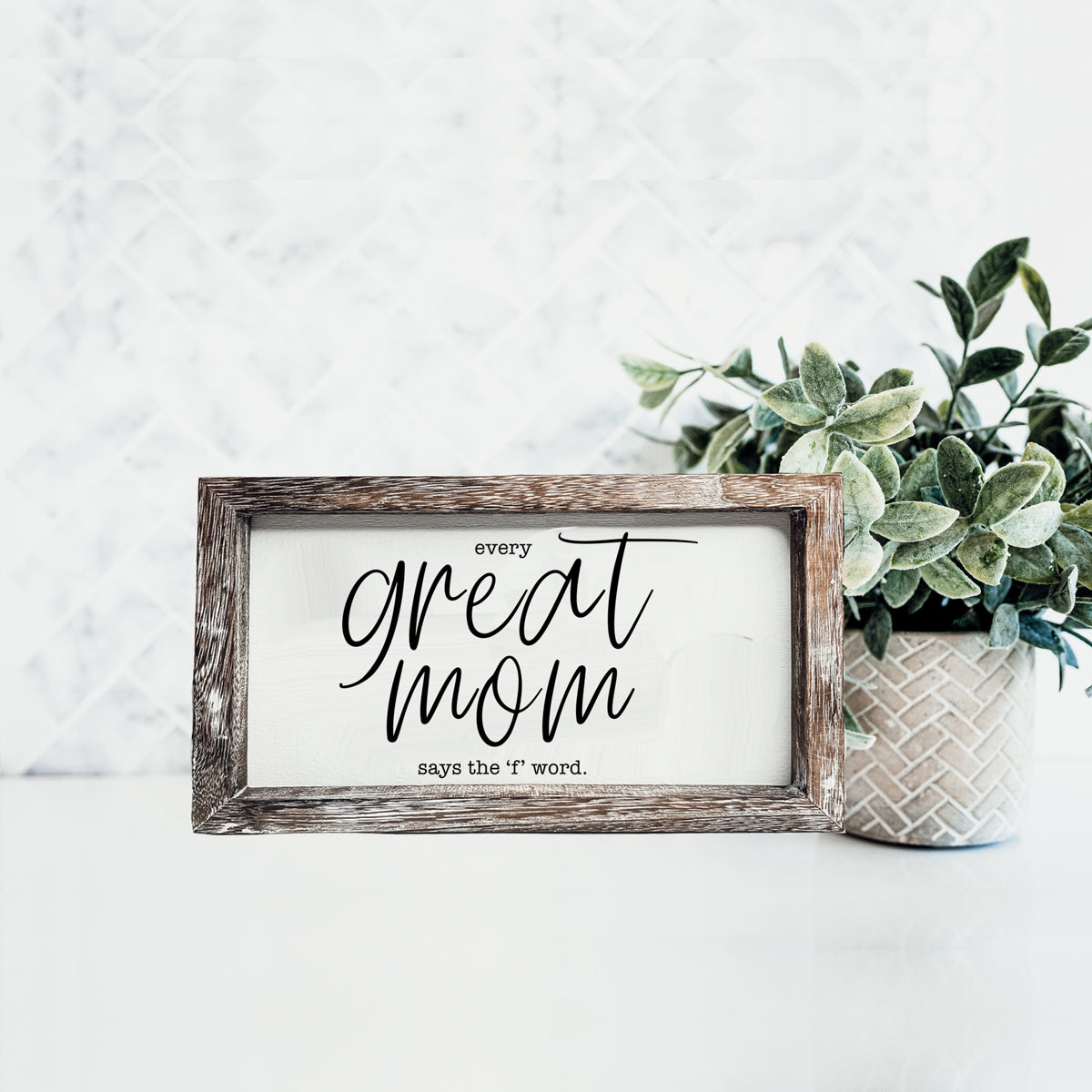 Great Mom sign in a weathered wooden frame with white panel and black script text beside a plant on Tampa Home & Garden Store