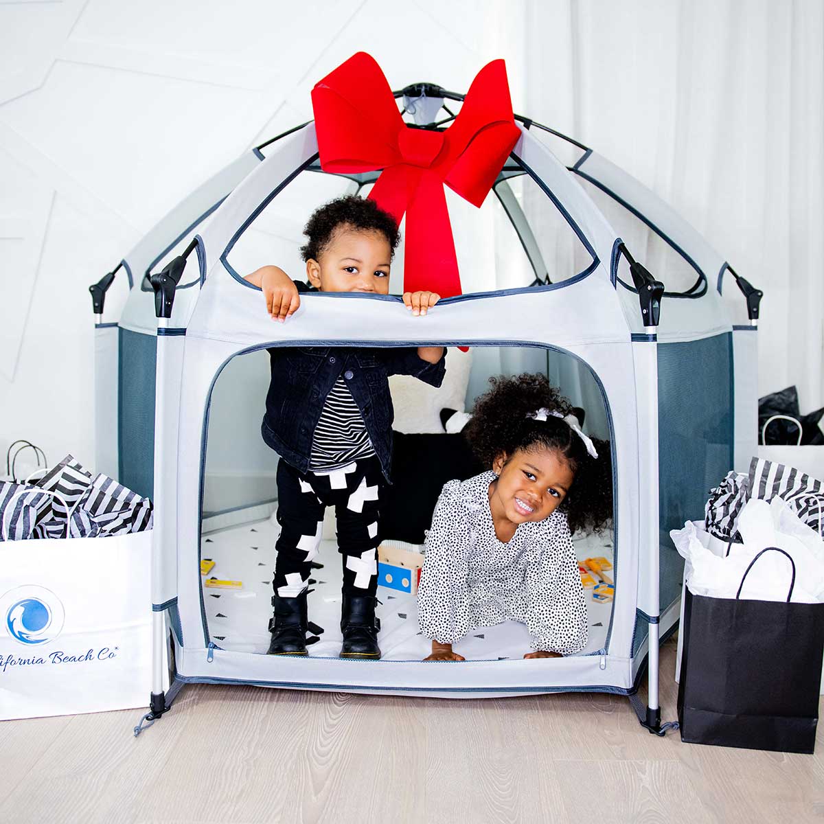 Pop 'N Go Playpen play yard in grey with a red bow and two kids inside California Beach Co LLC on Tampa Home & Garden Store