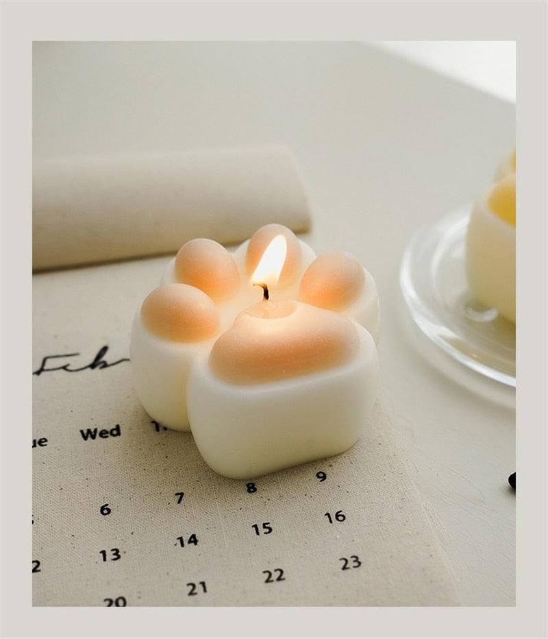 Teddy bear shaped scented candle, white with peach-tinted paw pads, lit wick on calendar on Tampa Home & Garden Store