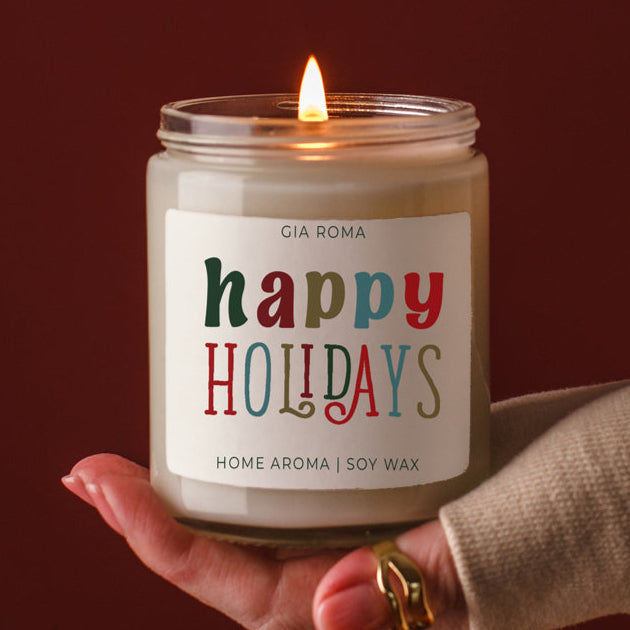 Happy Holidays candle by Gia Roma; soy wax, white jar with a colorful label, held in hand on Tampa Home & Garden Store