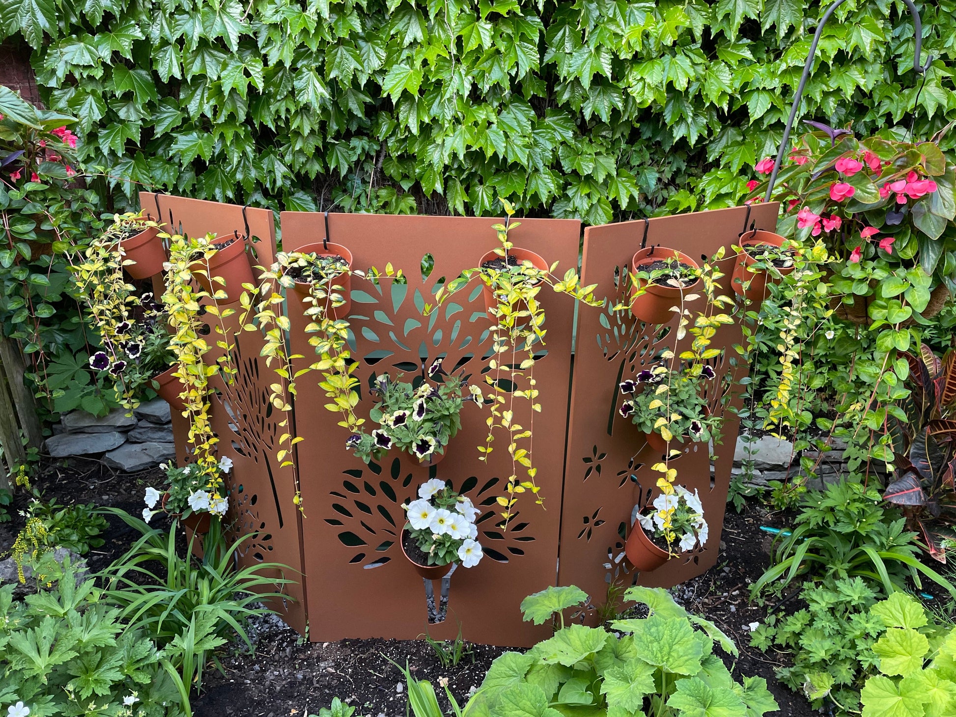 Outdoor privacy screen in rust-brown metal with leaf-cutout panels and hanging planters on Tampa Home & Garden Store