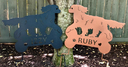 Two King Charles dog sculptures in blue and pink metal yard art by Rustica Ornamentals featuring IZZY and RUBY names on Tampa Home & Garden Store