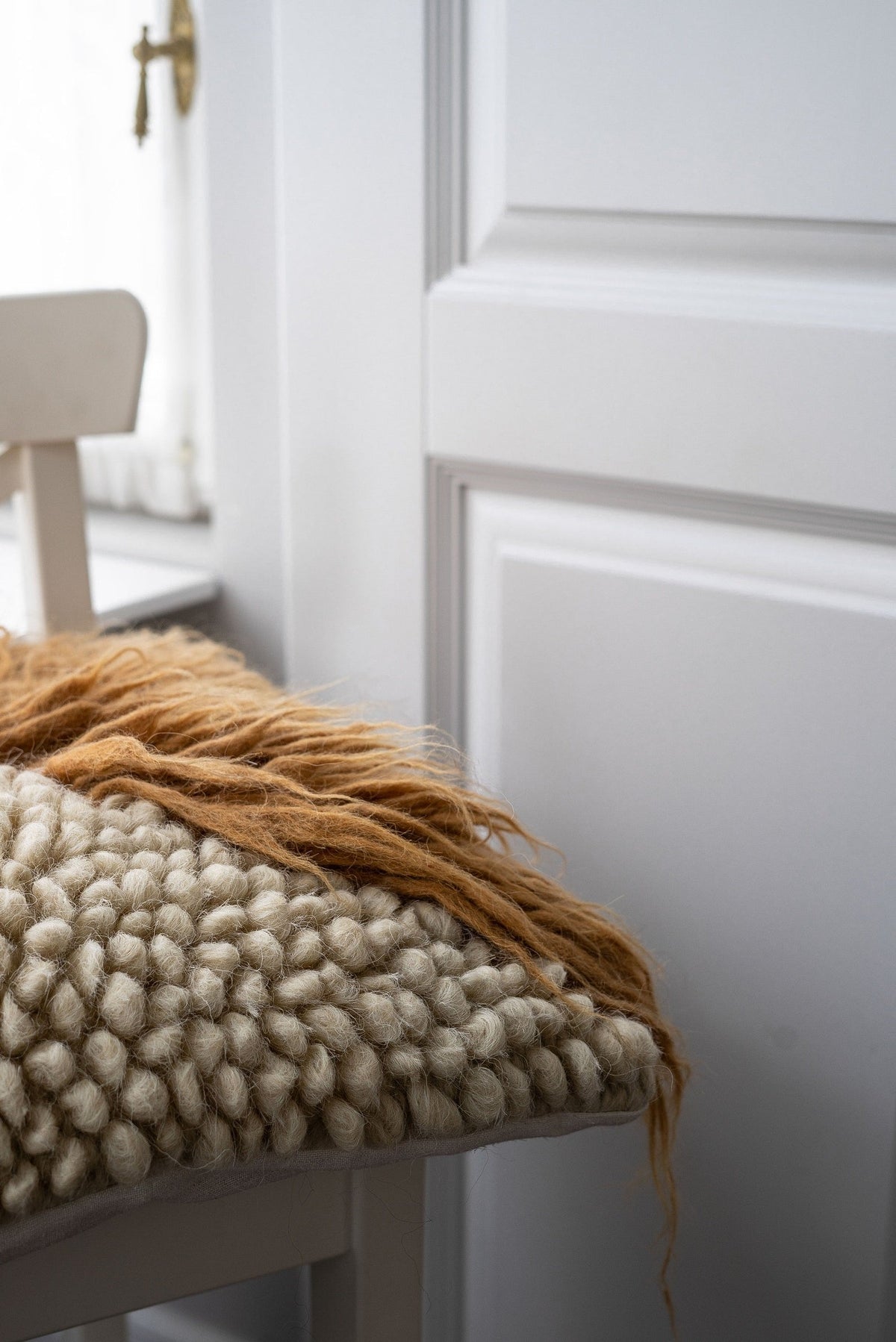 Pillow Forest Bark chunky knit throw pillow in cream and tan rests on a chair beside a white wall on Tampa Home & Garden Store