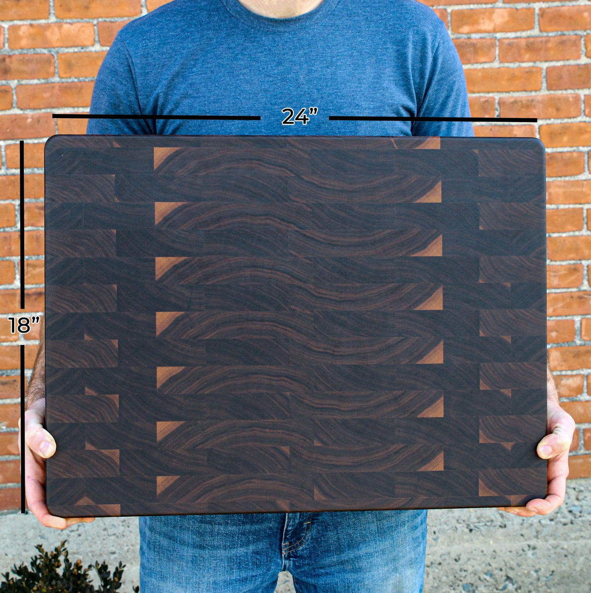 Walnut end-grain cutting board, large 24x18 inches, held by a person against brick wall on Tampa Home & Garden Store