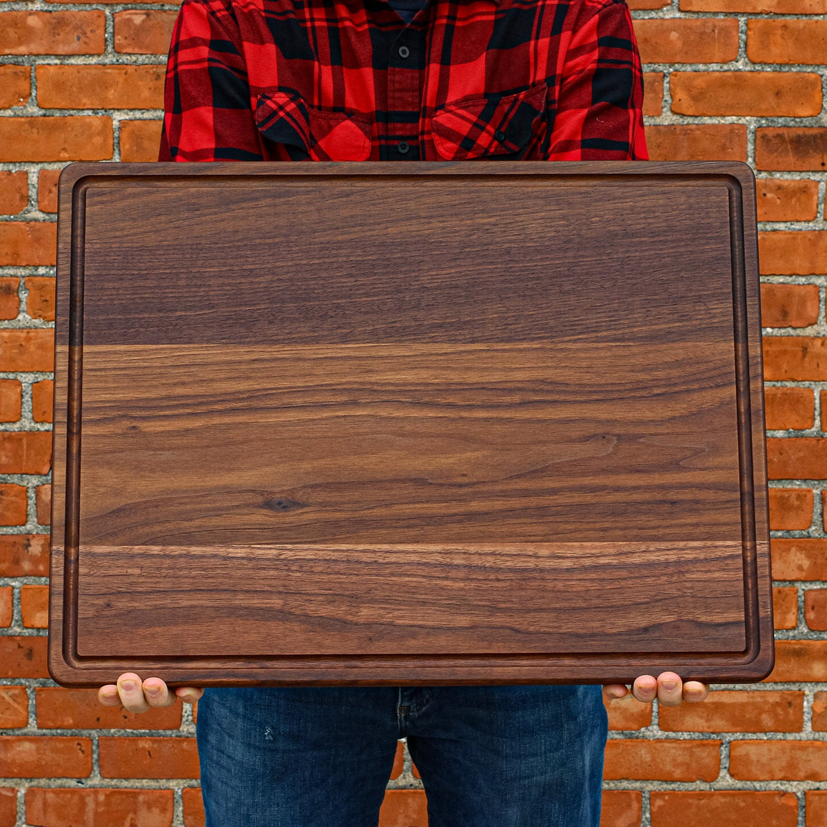 Extra large walnut cutting board 24x18 in with dark wood grain held by a person on Tampa Home & Garden Store