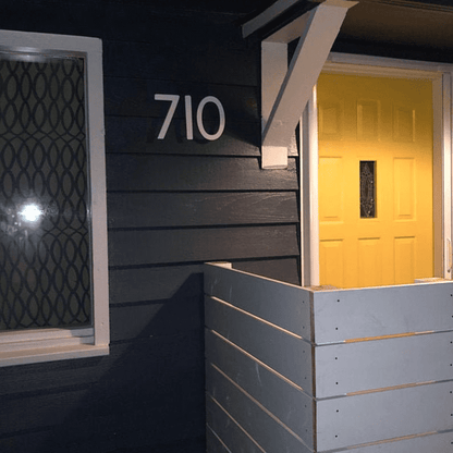 Mission Style house number 710, white metal numerals on dark siding near yellow door on Tampa Home & Garden Store