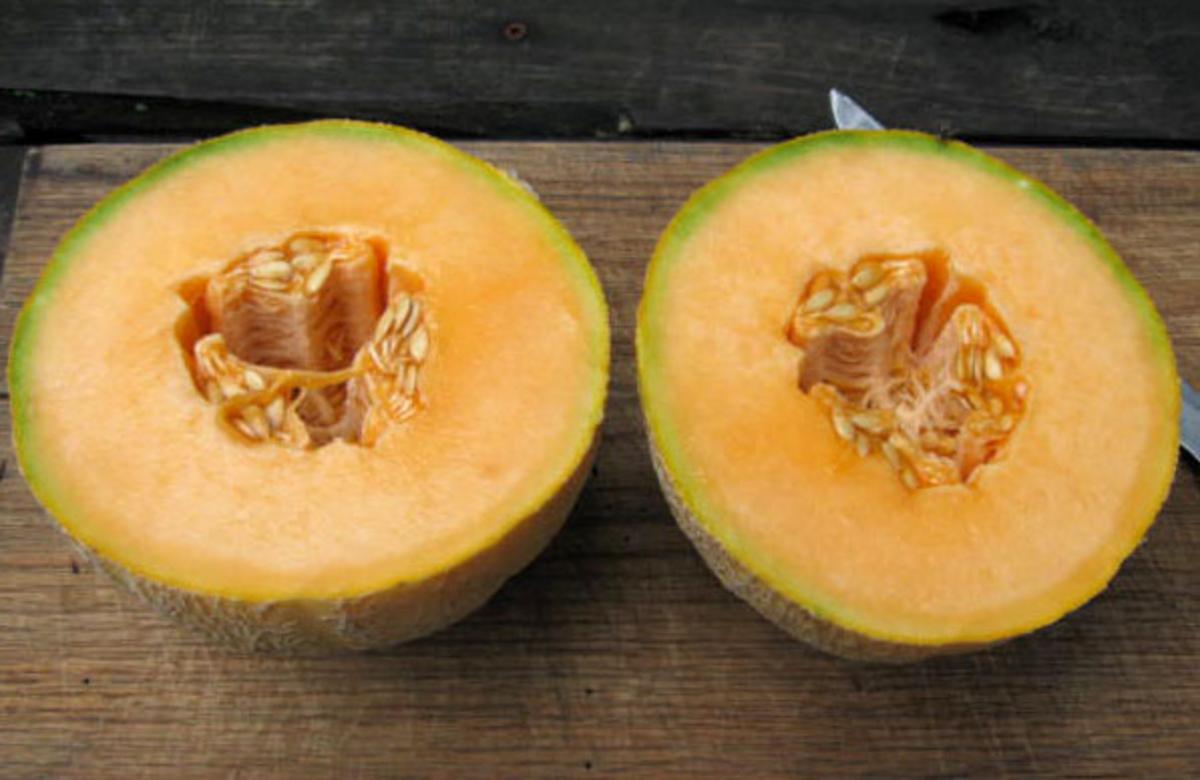 Two Kansas Muskmelon halves with orange flesh and seed cavity on a wooden cutting board on Tampa Home & Garden Store