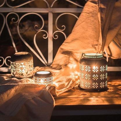 Metal Lantern Candle Holder set by RusticReach; 3 metal lanterns with floral cutouts casting warm candlelight on a wooden surface on Tampa Home & Garden Store