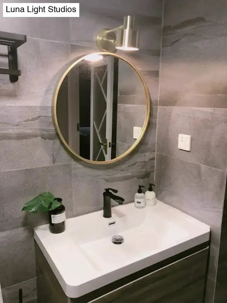 Mid-century gold metal wall sconce above circular gold-framed mirror over white bathroom vanity on Tampa Home & Garden Store