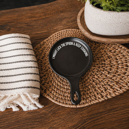 Gia Roma spoon rest, Lick the Spoon & Cook, black round with white text on woven placemat on Tampa Home & Garden Store