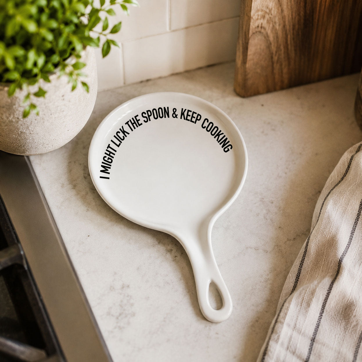 White ceramic spoon rest with curved handle and bold black text I MIGHT LICK THE SPOON & KEEP COOKING on Tampa Home & Garden Store