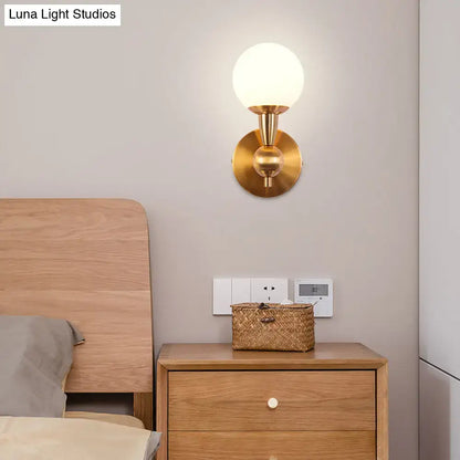 Gold hand-blown sconce with glass globe on brass backplate above a wooden nightstand on Tampa Home & Garden Store