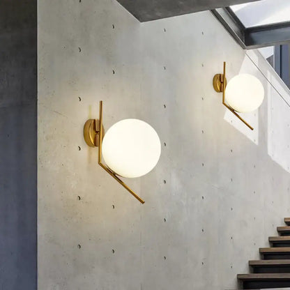 Pair of Decorbites gold mini globe wall sconces with white glass globes on concrete wall on Tampa Home & Garden Store