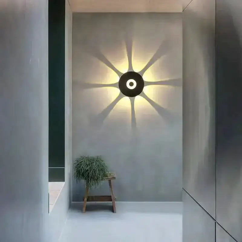 Modern black circular LED outdoor wall sconce casting a starburst glow on gray wall in a minimalist courtyard on Tampa Home & Garden Store