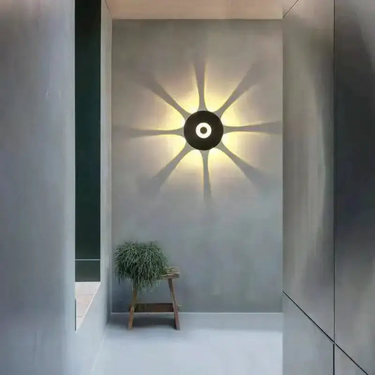 Modern black circular LED outdoor wall sconce casting a starburst glow on gray wall in a minimalist courtyard on Tampa Home & Garden Store