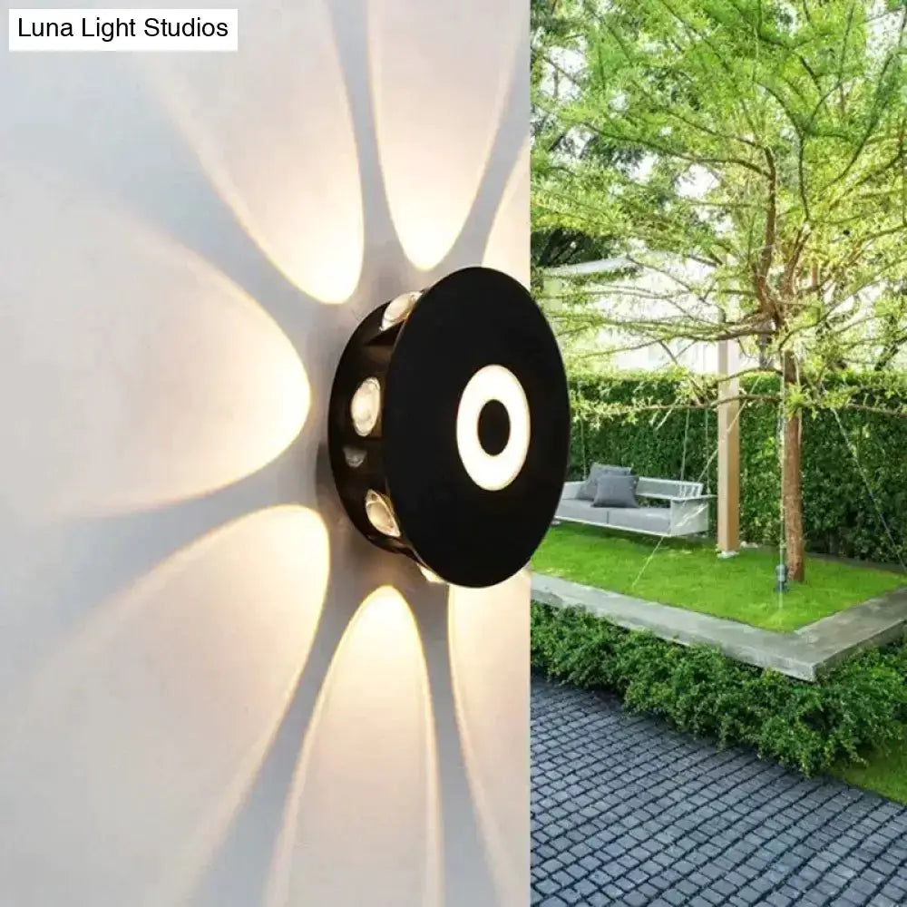Modern black circular LED outdoor wall sconce casting halo glow on white exterior wall on Tampa Home & Garden Store