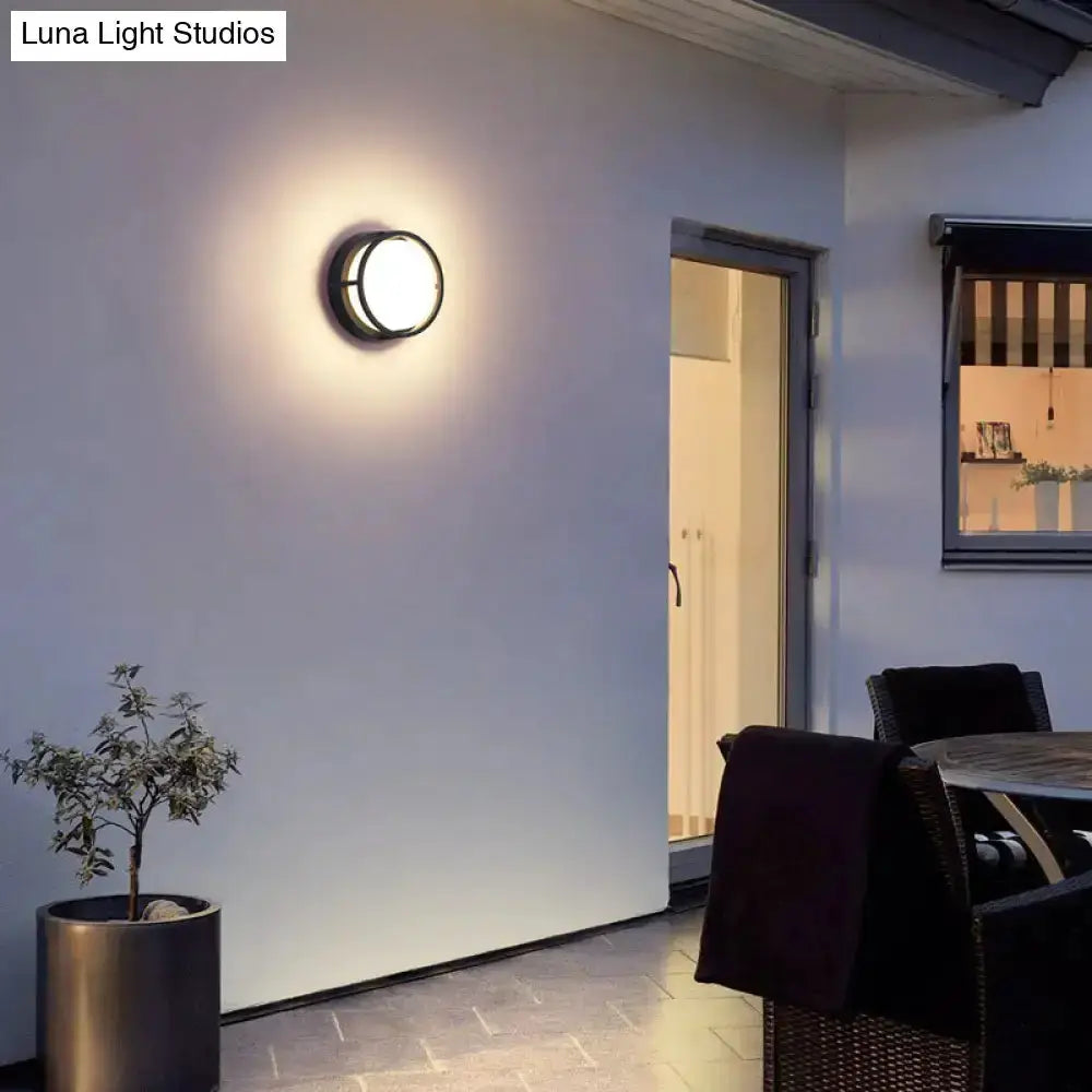 Black circular LED outdoor wall lamp emits warm glow on white exterior wall on Tampa Home & Garden Store