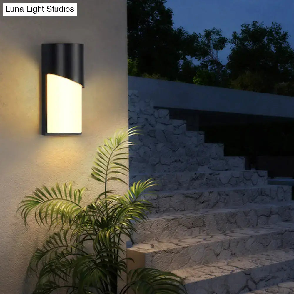 Black curved patio sconce by Decorbites on a stucco wall with warm light, tropical palm nearby on Tampa Home & Garden Store