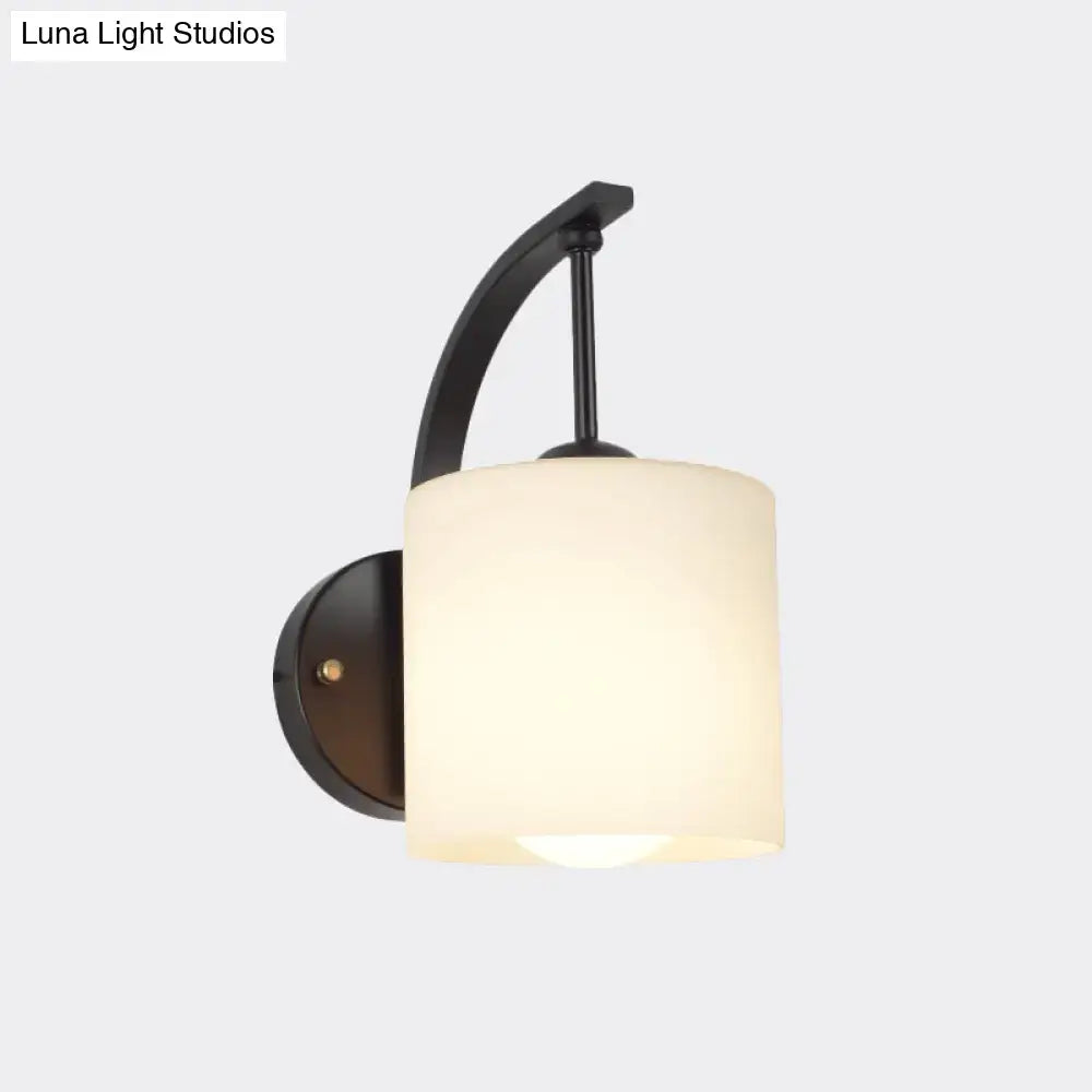 Black cylindrical opal glass wall sconce with curved metal arm on Tampa Home & Garden Store