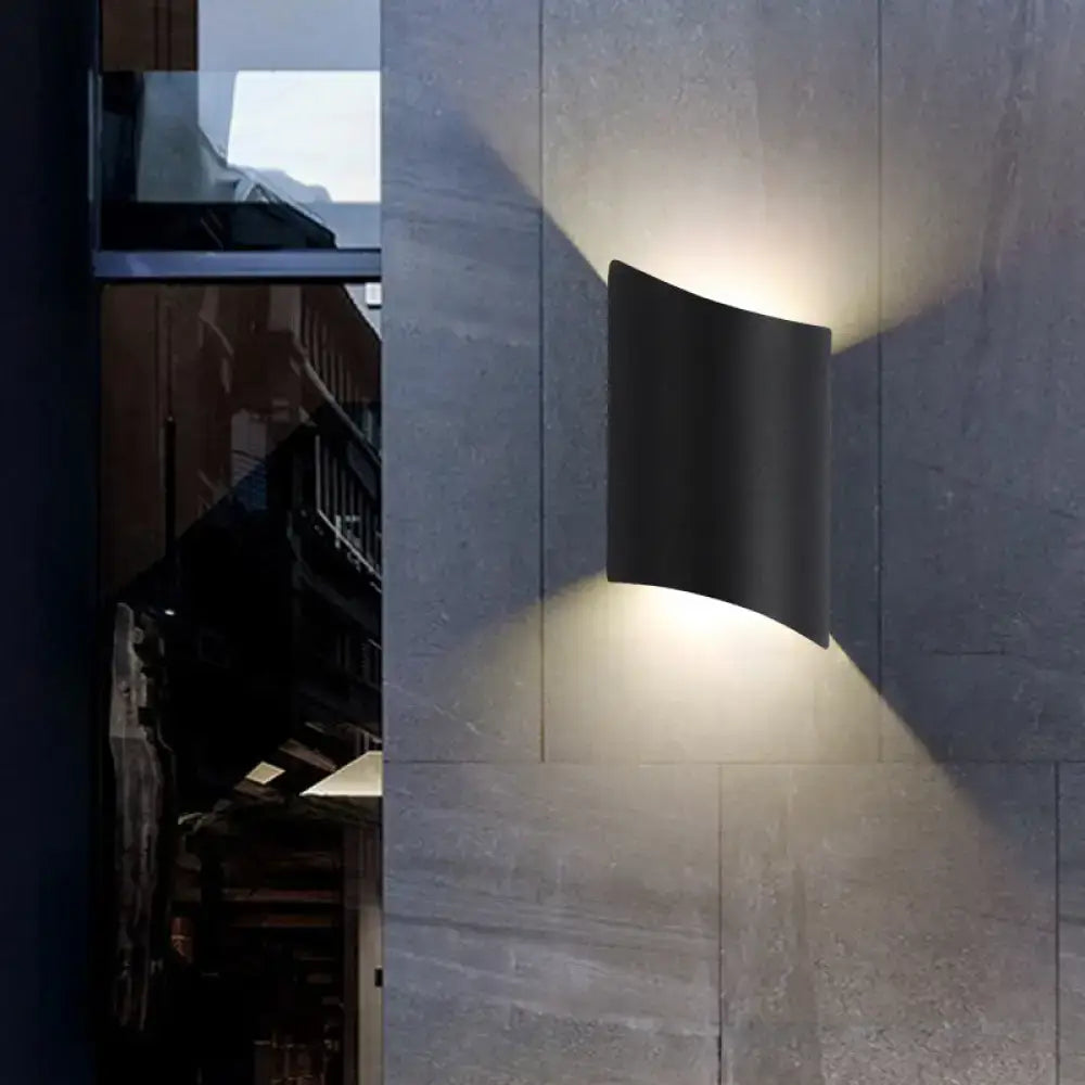 Black curved geometric patio wall light fixture illuminates stone wall on Tampa Home & Garden Store