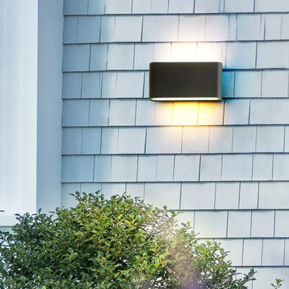 Black outdoor wall light by Decorbites mounted on gray siding, emits warm downward glow on Tampa Home & Garden Store
