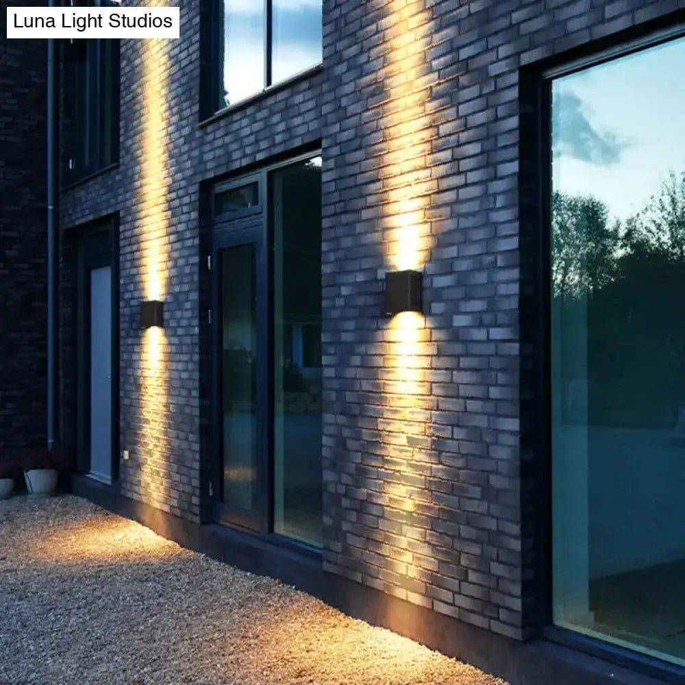 Two black metal shade outdoor wall sconces on brick exterior wall with warm uplighting on Tampa Home & Garden Store
