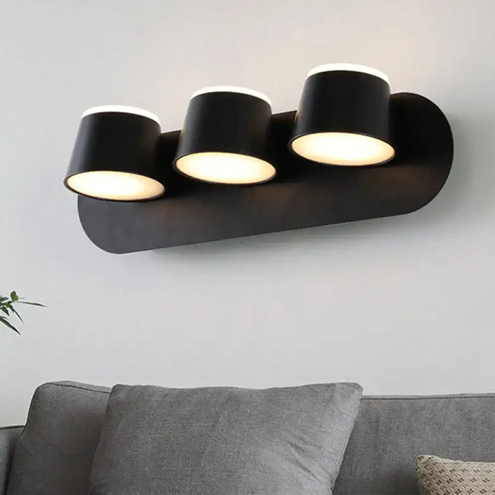 Black metal cone-shade 3-light wall sconce on a rounded backplate above a grey sofa on Tampa Home & Garden Store