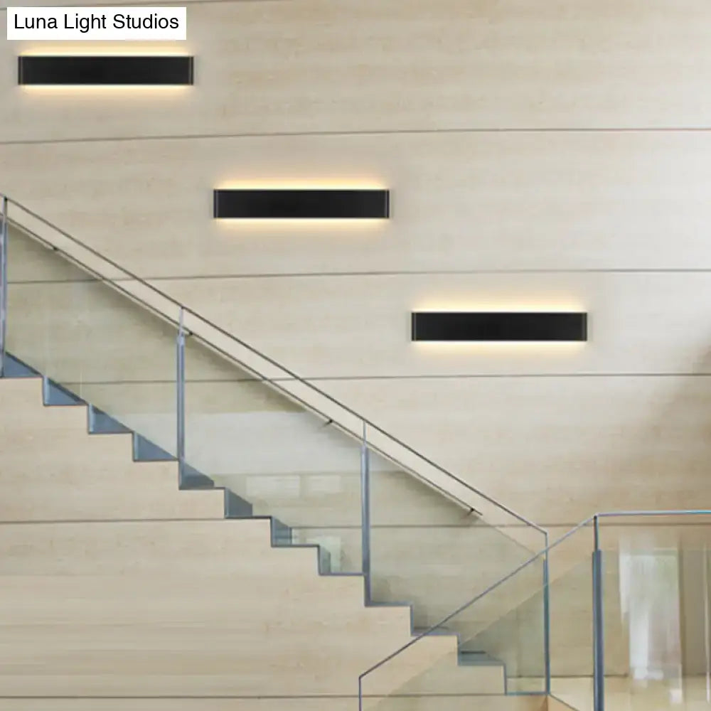 Three black rectangular wall lamps with warm glow on beige wall beside glass staircase on Tampa Home & Garden Store
