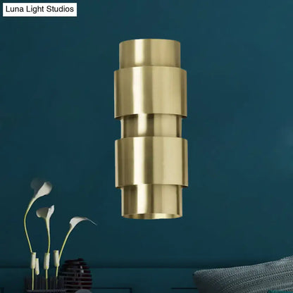 Brass metal shade sconce with stacked cylindrical tiers hanging against teal wall on Tampa Home & Garden Store